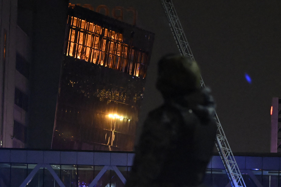 Сотрудник полиции на фоне горящего концертного зала Крокус Сити Холл, 20 марта 2024 года